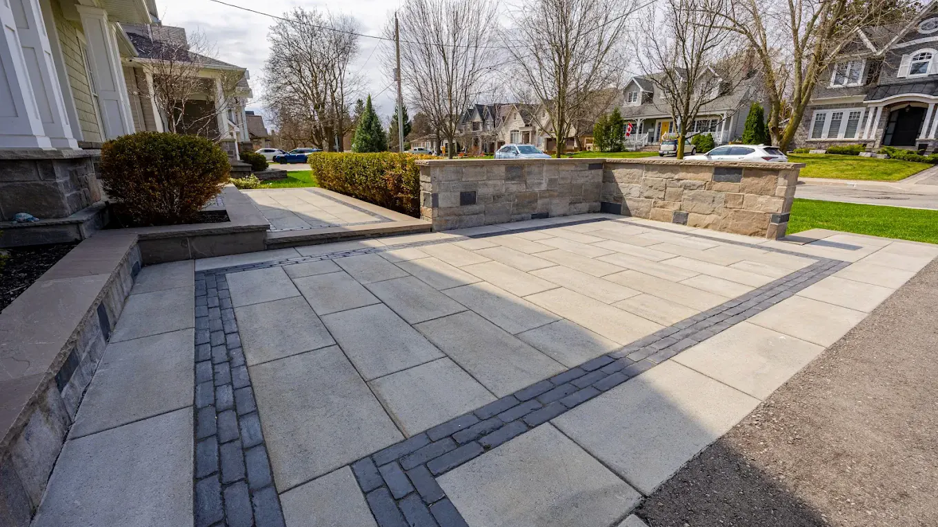 Interlocking driveway in large-format slab pavers with a double charcoal border and a stone seat wall