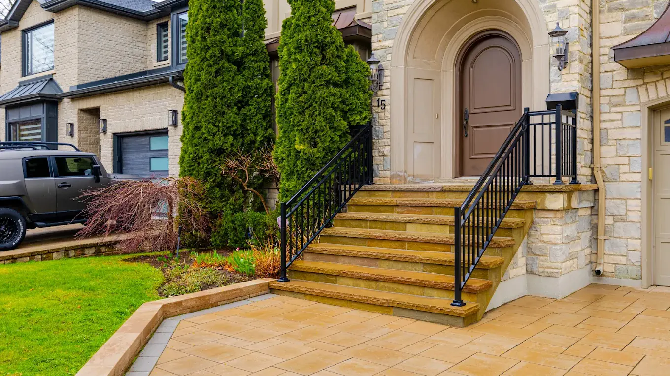 Natural stone front entrance steps with a black aluminum railing rising from a paver landing