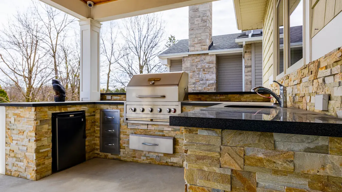 Covered outdoor kitchen with stacked stone veneer, honed granite counters and a built-in gas grill