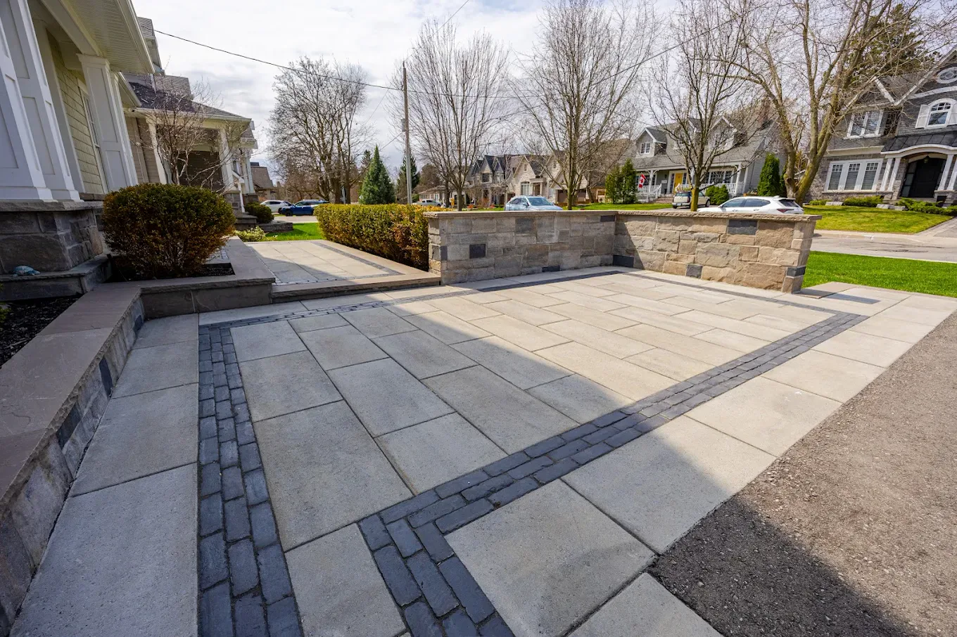Wide interlocking driveway in large-format slab pavers with a double charcoal border and a natural stone seat wall