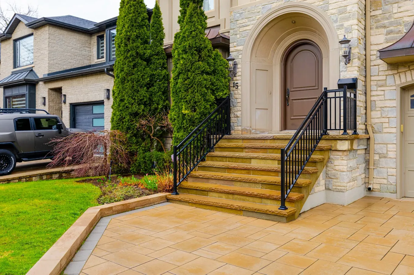 Natural stone front entrance steps with an aluminum railing above a low seat wall and paver landing