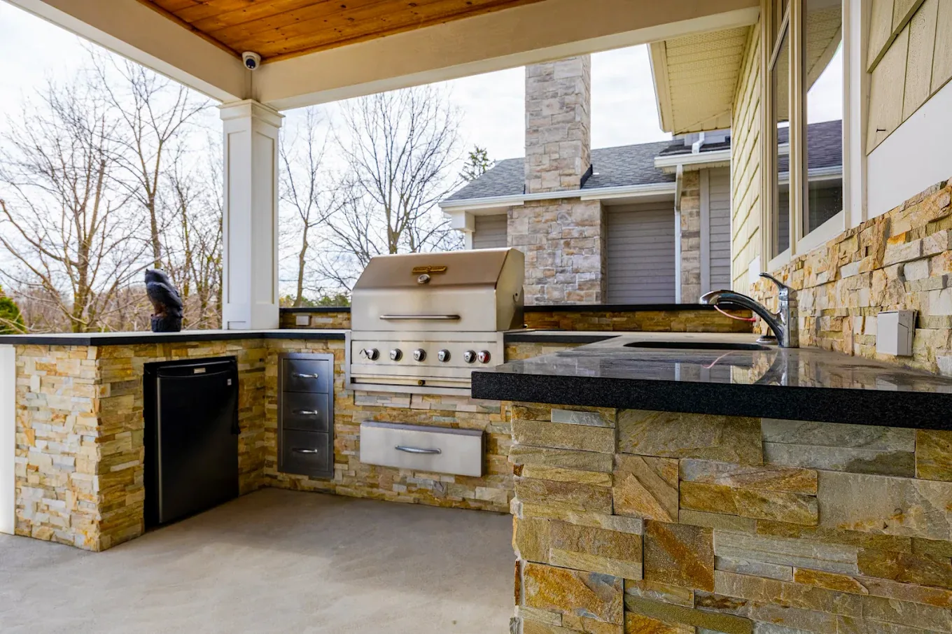 Covered outdoor kitchen with stacked stone veneer, granite counters and a built-in gas grill